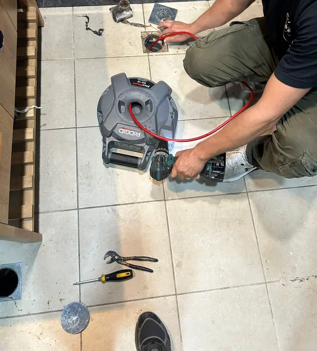 מכונה לפתיחת סתימות מחוברת לפתח ניקוז ברצפת חדר רחצה